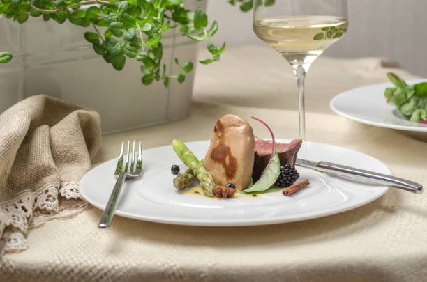 Assiette avec du foie gras, de la viande et des asperges et un verre de vin blanc