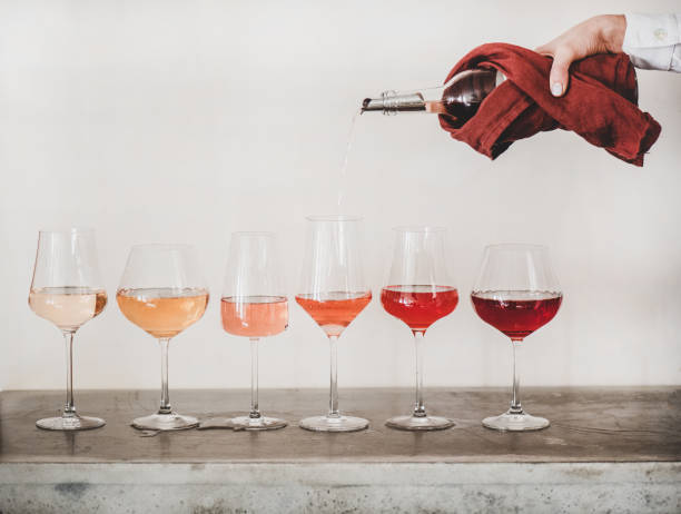 Verres de rosé alignés de différentes couleurs et bras qui sert un verre de rosé au dessus d'un verre.